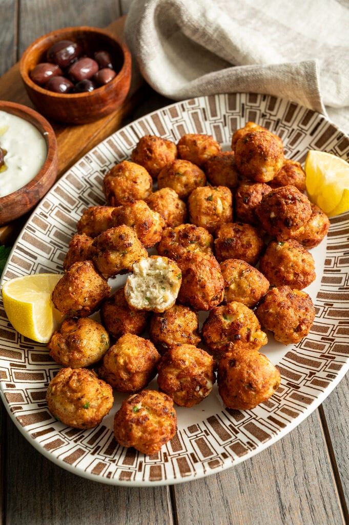 Greek chicken meatballs with feta on a white and brown platter, surrounded by lemons, tzatziki and olives.