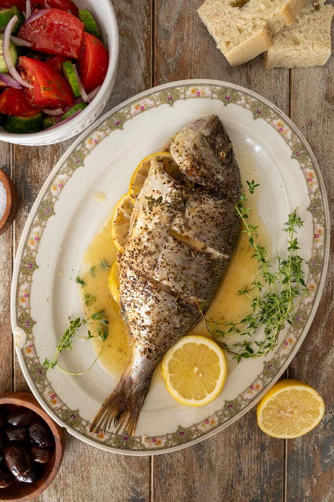 The baked sea bream on a white platter, surrounded by juices, lemon slices and fresh thyme.