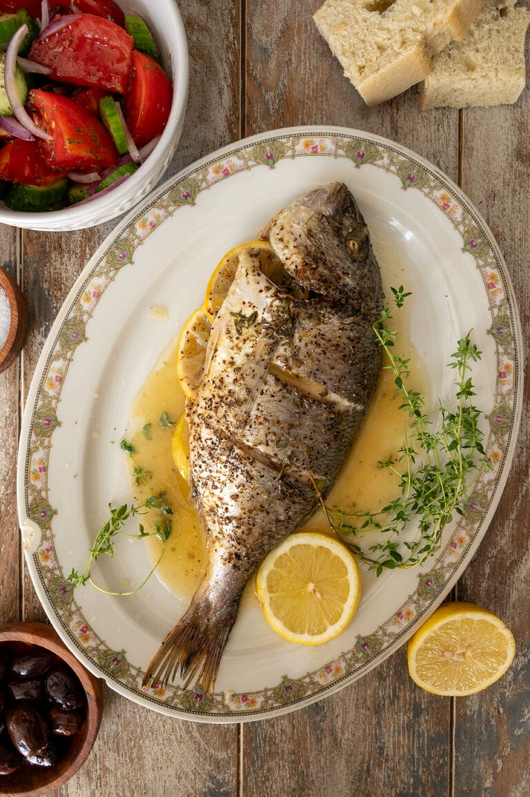 The baked sea bream on a white platter, surrounded by juices, lemon slices and fresh thyme.