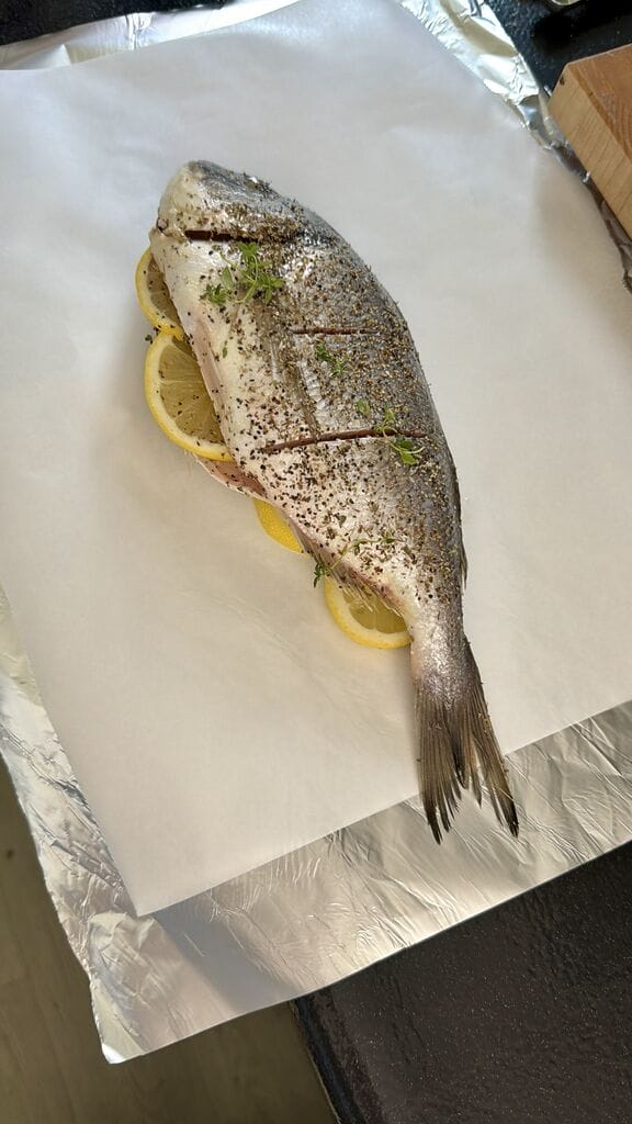 The fish has been prepared for baking, it is sitting on a layer of parchment paper and aluminum foil.